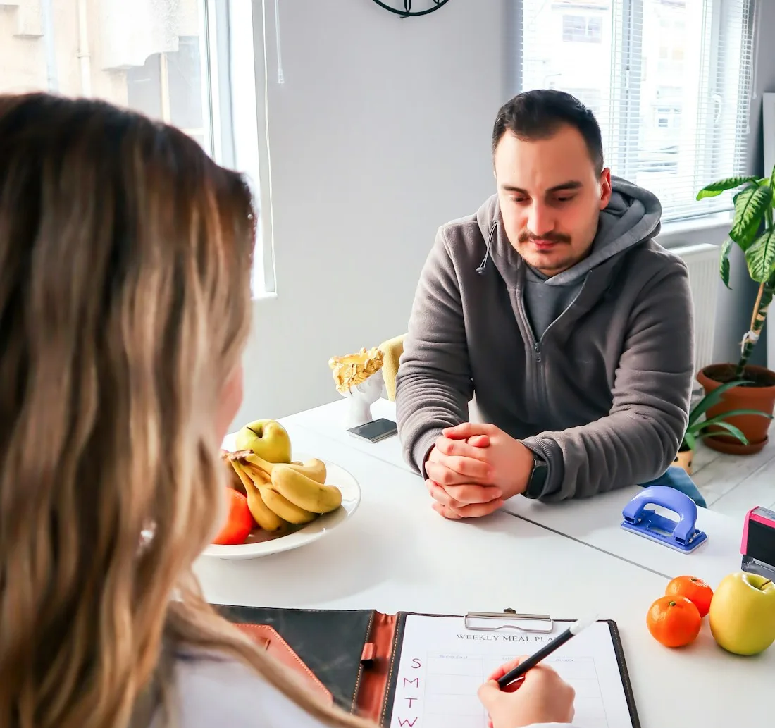 Une diététicienne prend des notes face à son patient, des fruits sur la table